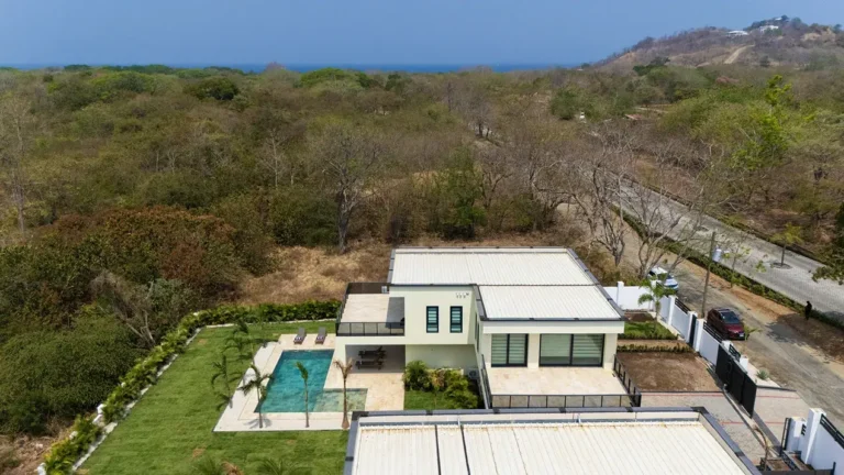 Aerial view of Casa de Acero among dry forest with the ocean on the horizon.