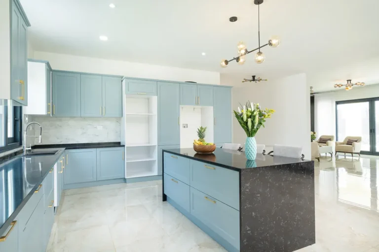 Kitchen with pale blue cabinetry, a dark stone island and modern pendant lights.