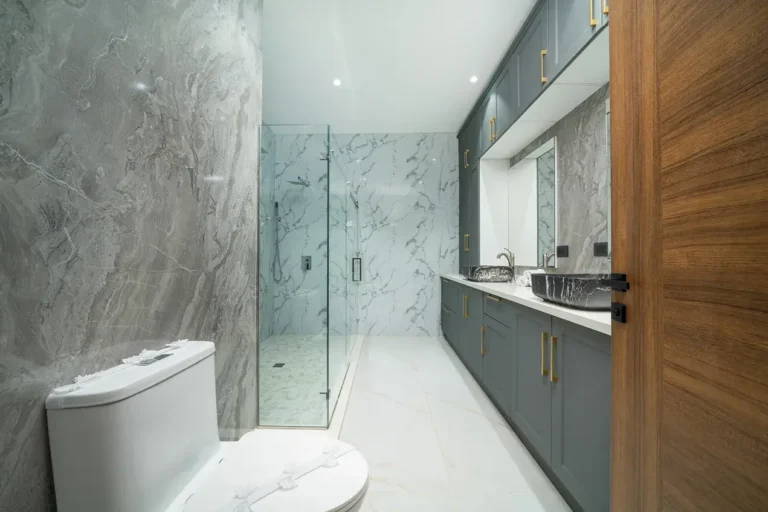 Bathroom with marble-look walls, a glass walk-in shower and dark vanity.