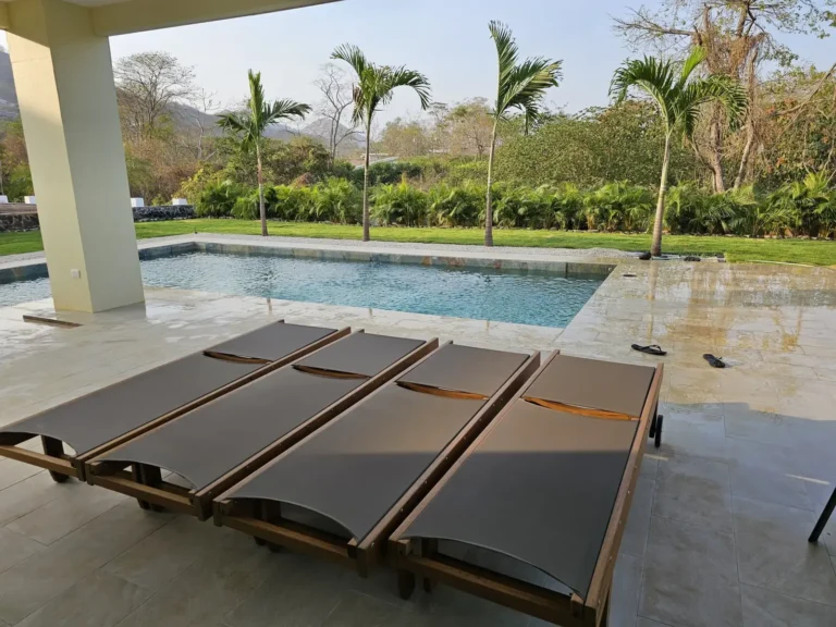 Covered pool deck with sun loungers looking out to palms and the garden.