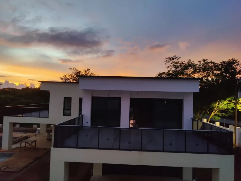 Rear facade and glass balcony of Casa de Acero under an orange sunset sky.