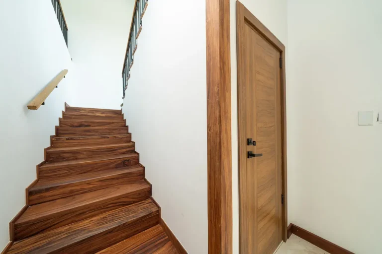 Hardwood staircase with a wooden handrail beside a white wall.
