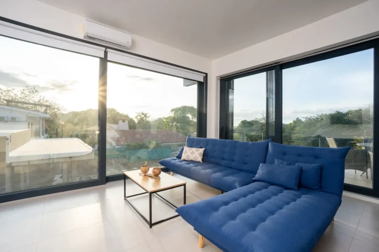 Apartment living area with a blue sectional sofa and sliding doors framing the trees outside.