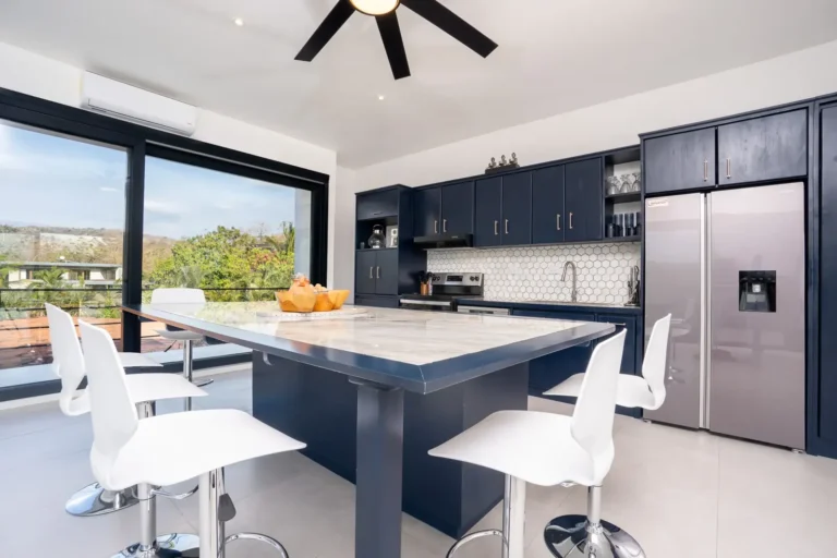 Kitchen island with white bar stools beside large windows looking out to the hills.