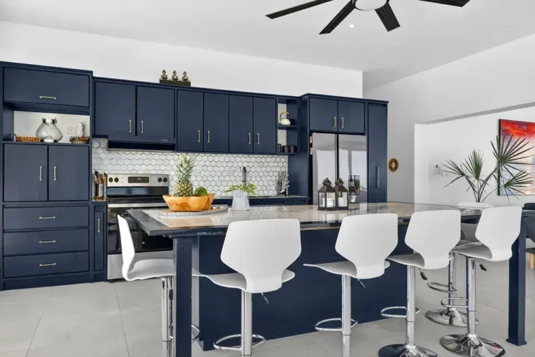 Navy-blue kitchen with a long island, white stools and patterned backsplash.