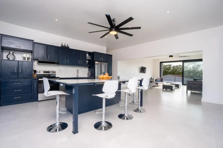 Open-plan kitchen with navy cabinets, a long island with white stools and floor-to-ceiling windows.