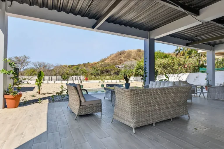 Covered outdoor lounge with wicker sofas facing the pool and hillside.