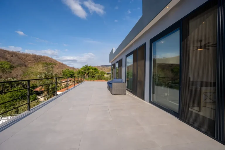 Large tiled terrace with a steel railing and sliding glass doors overlooking the hills.