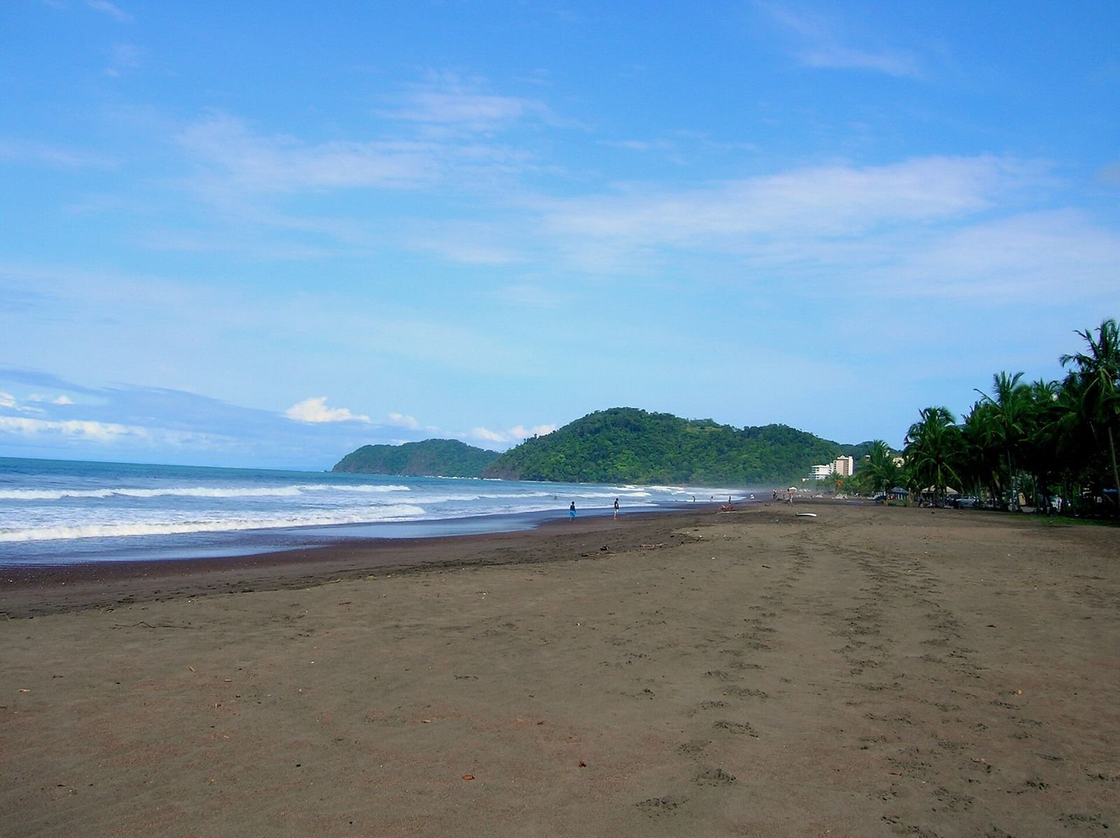 The long sandy beach at Jacó with green hills at the end of the bay.