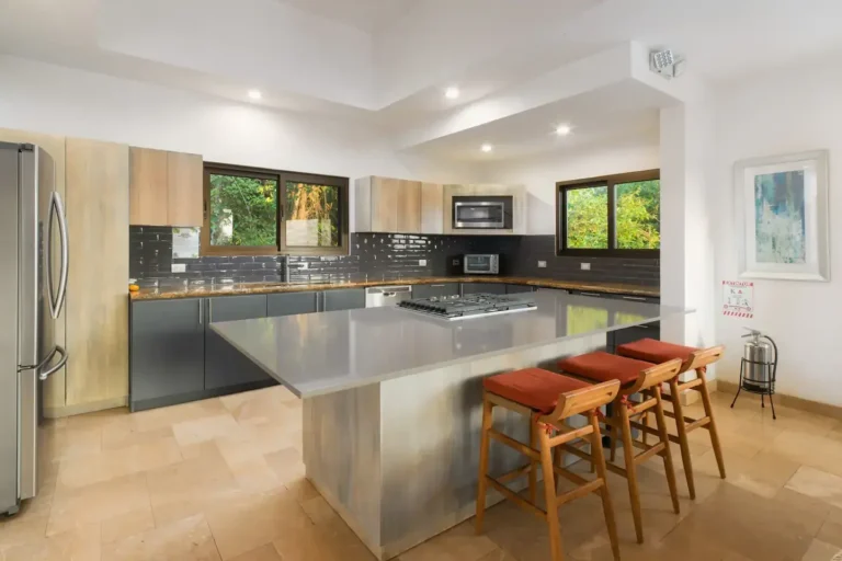 Kitchen with a stainless-steel island, red stools and forest views.
