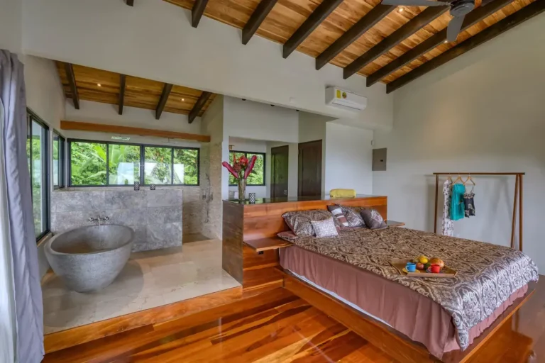 Bedroom with exposed wood beams and a freestanding stone bathtub by the windows.