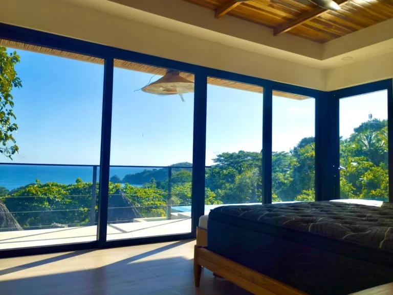 Primary bedroom at Villa Pochote with a wall of glass facing the ocean and forest